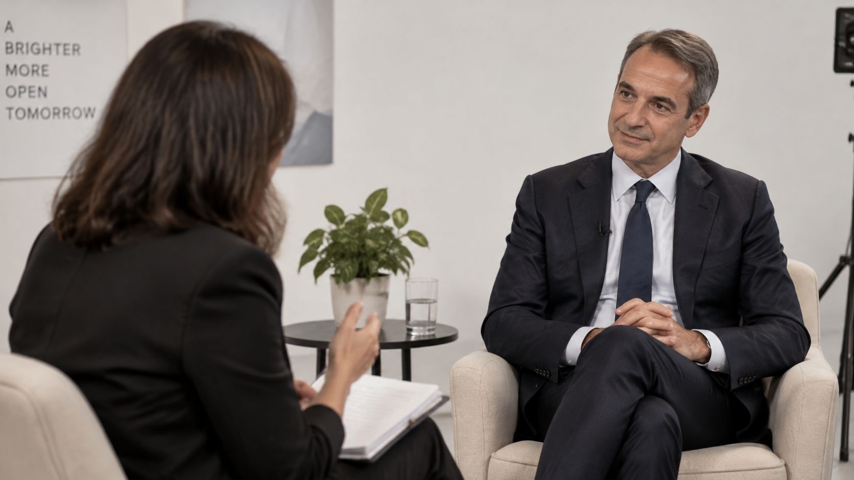 Ein Mann im Anzug gibt in einem professionellen Studio einer Interviewerin ein aufschlussreiches Gespräch.